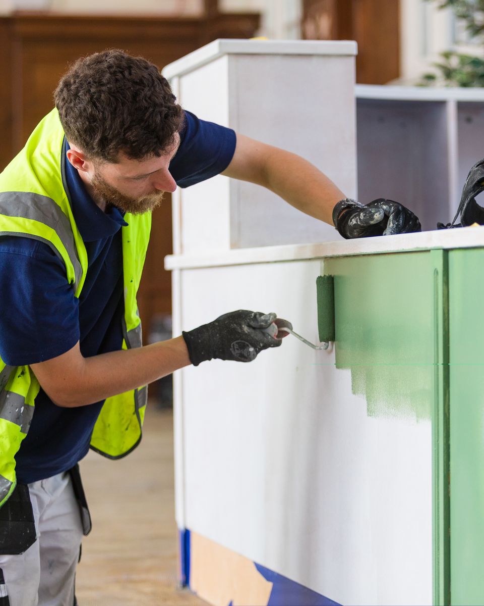 Collab decorator cutting in green paint on a curved library reception desk